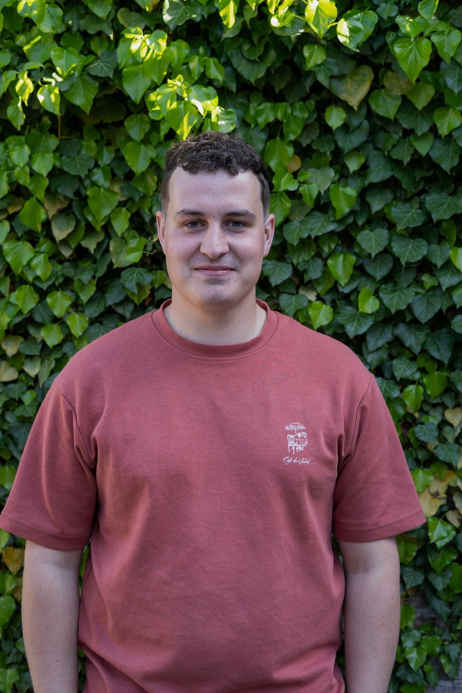Tobias, glimlachend voor een muur met klimop